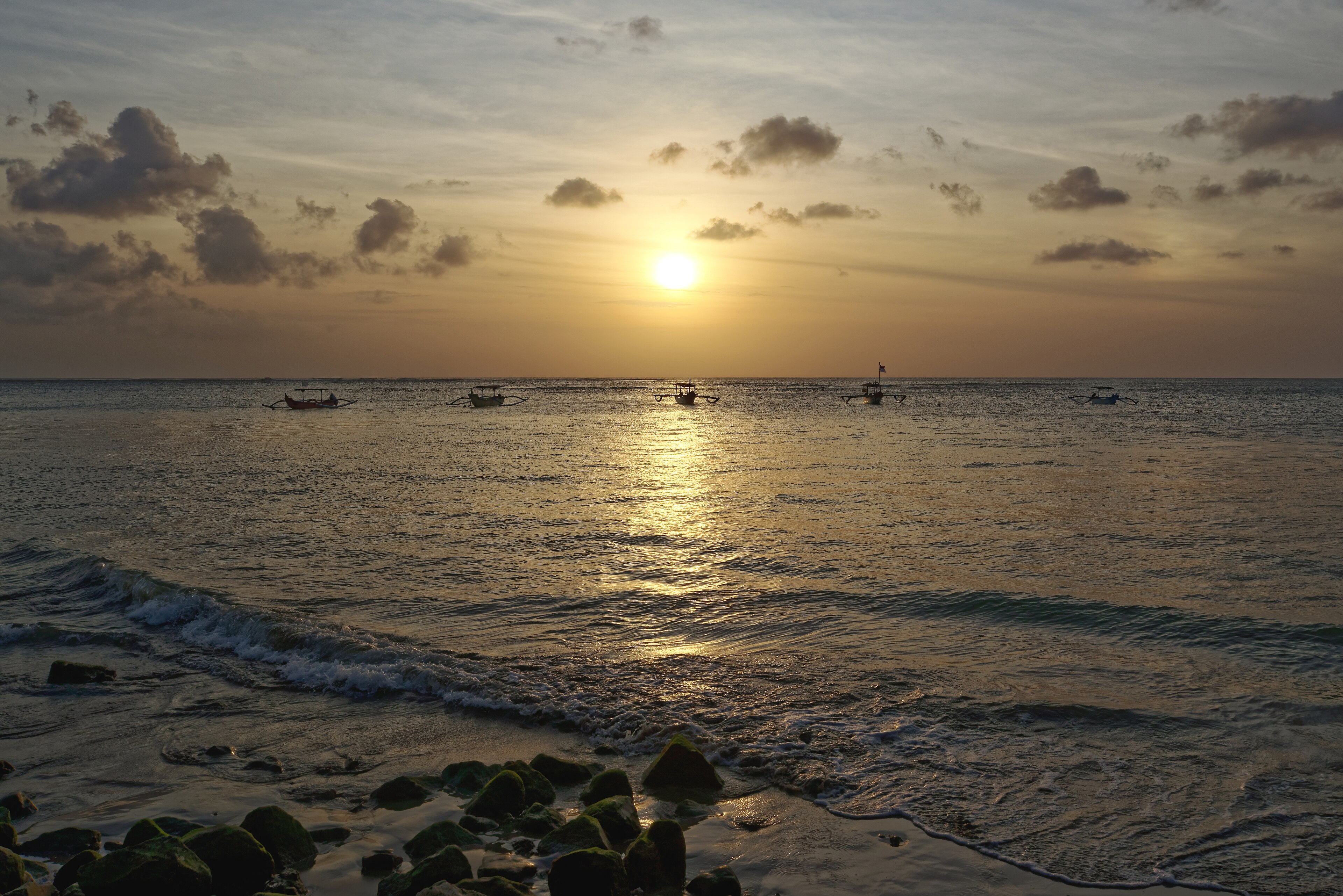 Traditional fishing boats silhouetted against a golden sunset over the ocean at Kuta Beach, Bali