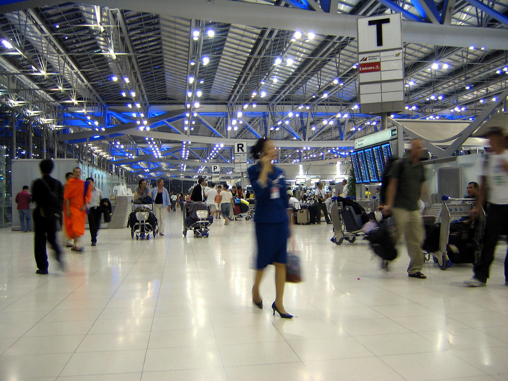 Travelers with luggage trolleys inside Suvarnabhumi Airport departures hall in Bangkok